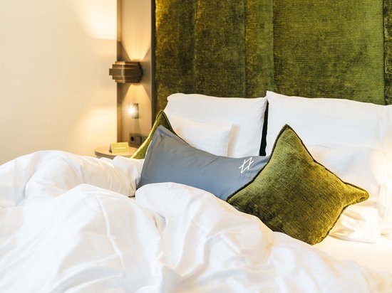 Reine Urlaubsfreude in Ihrem Hotel in St. Anton Gemachtes Bett mit weißen Laken und grünen Kissen vor grünem Polsterkopfteil