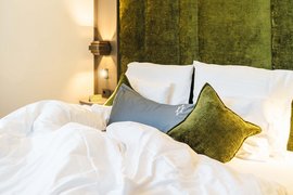 Info on hikes in St. Anton am Arlberg and more Made bed with white sheets and green pillows against a green upholstered headboard