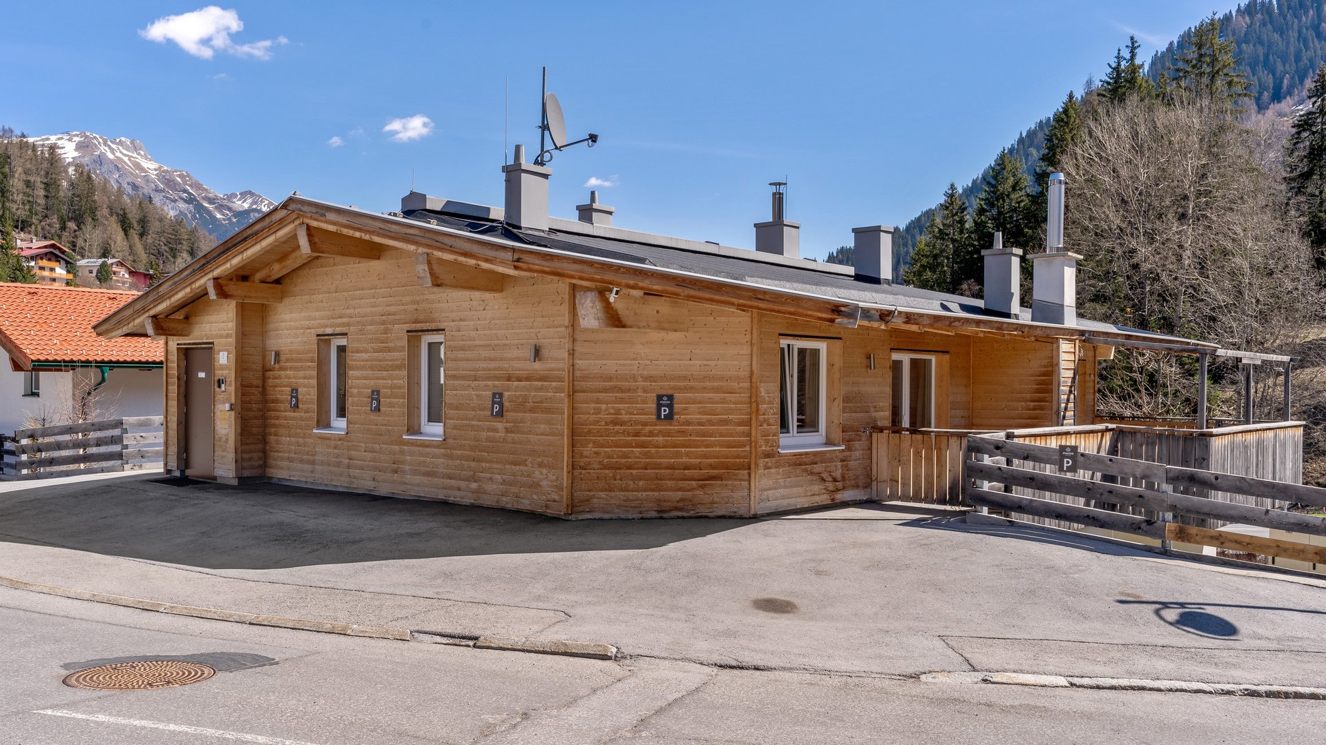 Stanton Lodge – Apartments in St. Anton am Arlberg Wooden house in mountain landscape with snowy peaks and clear sky