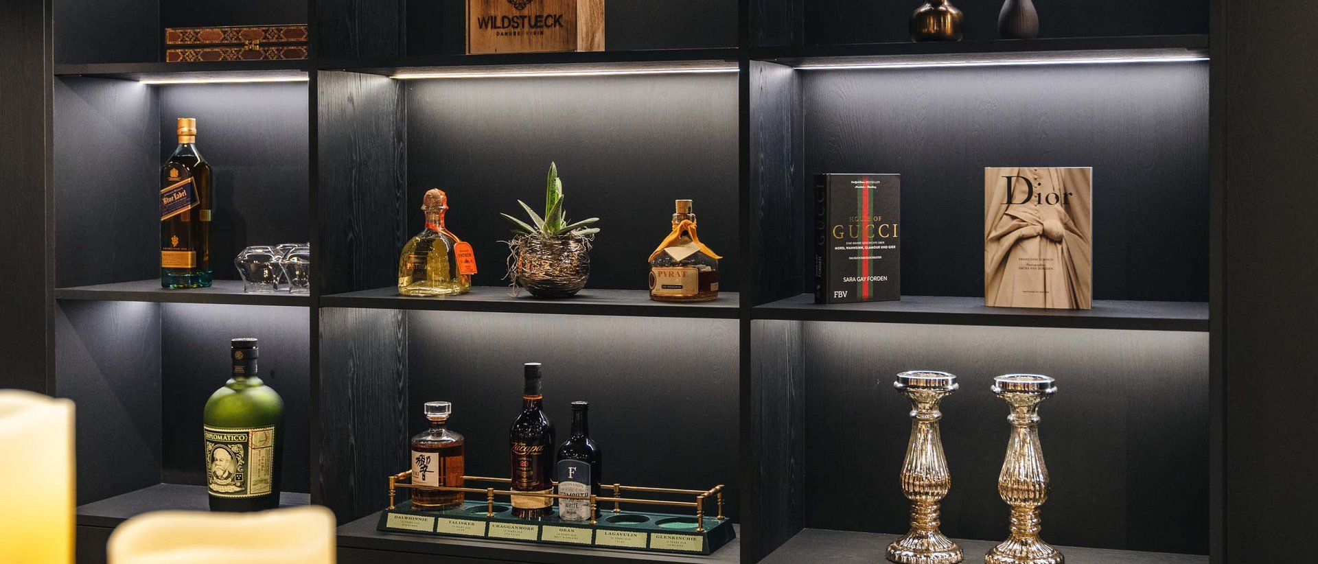 Reine Urlaubsfreude in Ihrem Hotel in St. Anton Beleuchtetes Regal mit Spirituosen, Büchern, Kerzen und Dekoration in modernem Raum