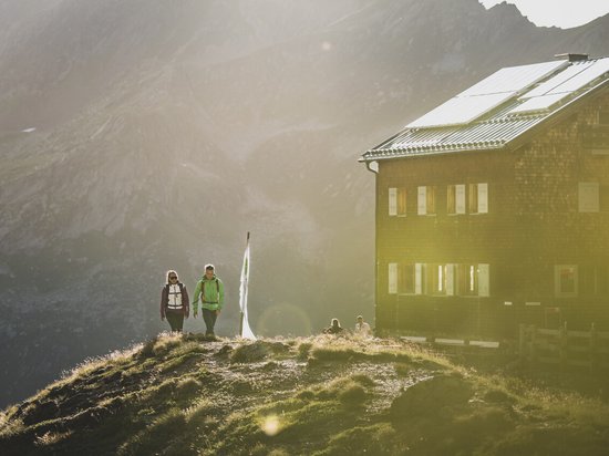 Winter hiking at Mt Arlberg Hikers near a mountain hut with sunlight and mountains in the background