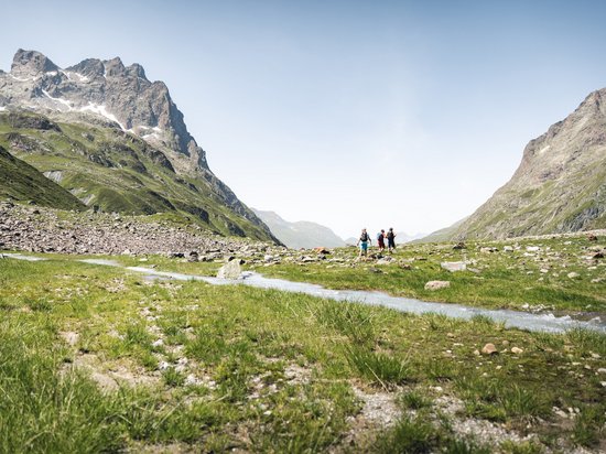 Delicious indulgence in a glass Three hikers in a green valley with mountains and a stream under a blue sky